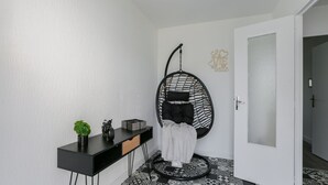 Una habitación moderna con suelo a cuadros blanco y negro, un escritorio negro con una planta, una silla colgante y una puerta blanca.
