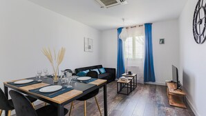 Una sala de estar moderna con comedor, que incluye un sofá, un televisor y una pequeña mesa con una computadora.