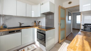 A modern kitchen with white cabinets, a wooden countertop, a built-in oven, and a dishwasher. - Callisto - Appartement Vue Mer (Luc-sur-Mer)