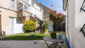 A courtyard with a small table and chairs, a potted plant, and a staircase leading to an upper floor. - Callisto - Appartement Vue Mer (Luc-sur-Mer)