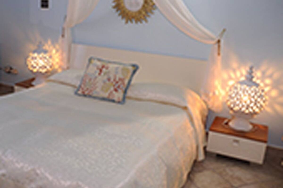 Quarto com cama de dossel, duas luminárias de cabeceira e um sol decorativo na parede.