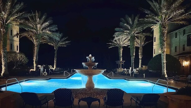 A nighttime swimming pool with a central fountain, surrounded by palm trees and lounge chairs. - 2-BR large private fenced courtyard-close to entrance & pool / hot tub (Saint Augustine)