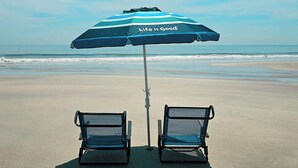 A beach with two empty chairs and a striped umbrella with the text "Life is Good". - 2-BR large private fenced courtyard-close to entrance & pool / hot tub (Saint Augustine)