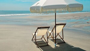 A beach with two beach chairs and a large white umbrella.
