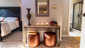 A hotel room with a dark wooden bed, a decorative mirror, a small table with candles, and a view of the bathroom.
