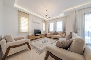 A modern living room with a sofa set, a TV, and a chandelier.