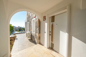 A hallway with a stone wall, a door marked with a large letter, and a view of a pool and outdoor seating.