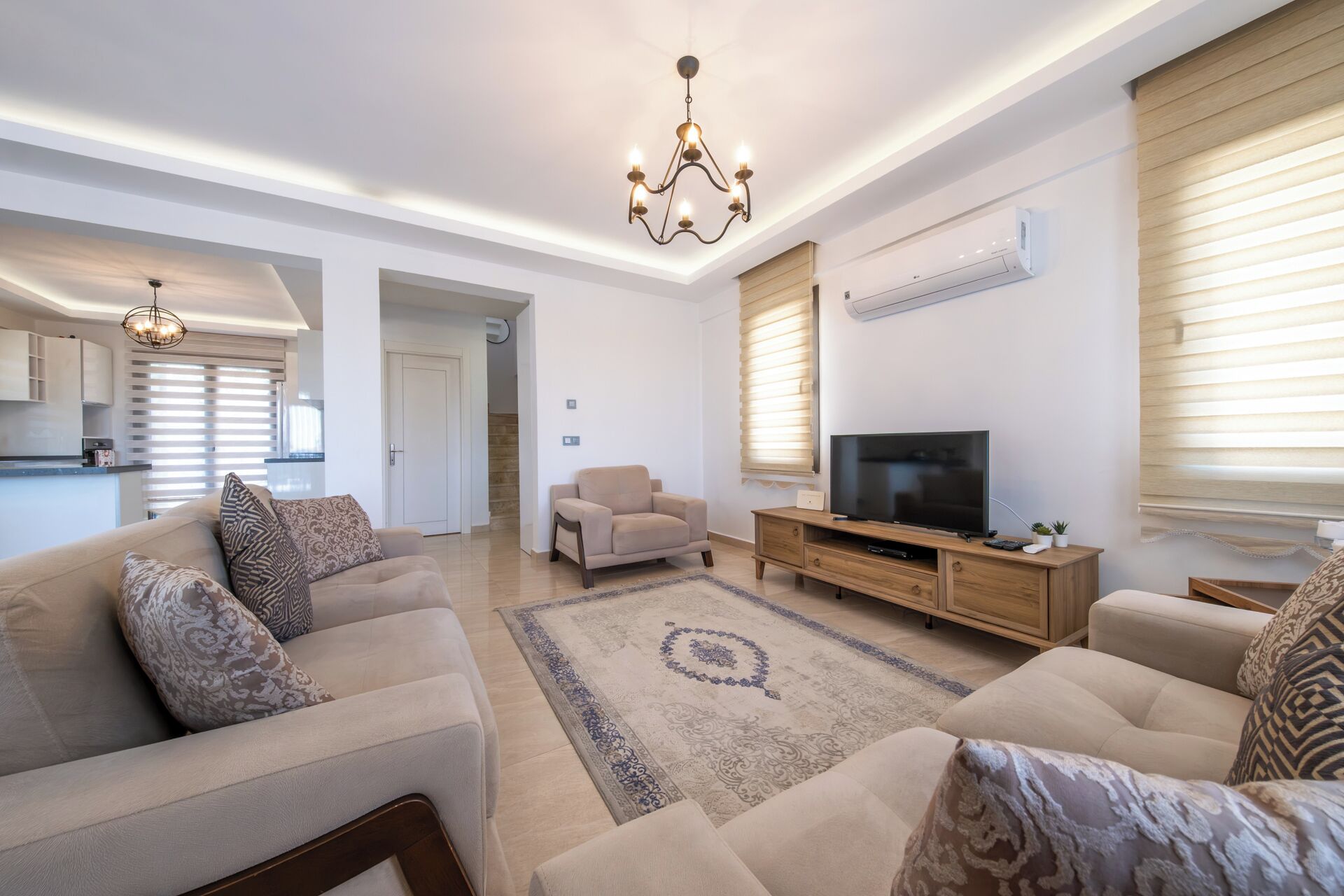 A modern living room with a sofa set, a TV, and a chandelier.
