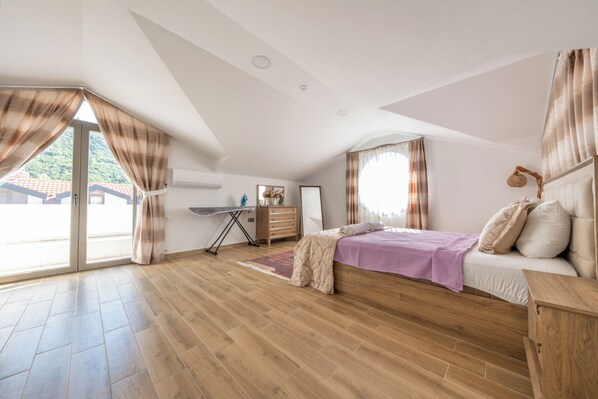 A bedroom with a bed, a dresser, an ironing board, and a window with curtains.