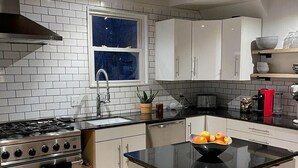 Une cuisine moderne avec des meubles blancs, un îlot central doté d’un plan de travail noir, des appareils électroménagers en acier inoxydable et un plafond en bois.