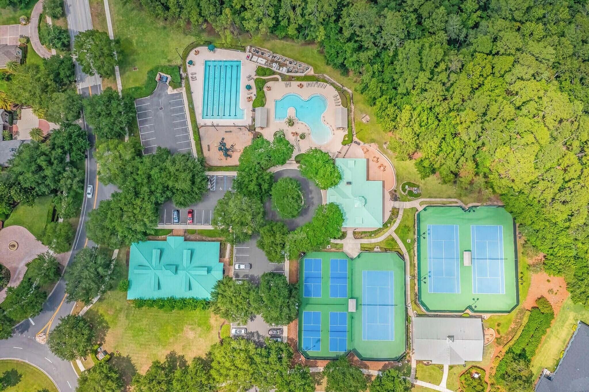 An aerial view of a resort with a swimming pool, tennis courts, and a large building with a green roof.