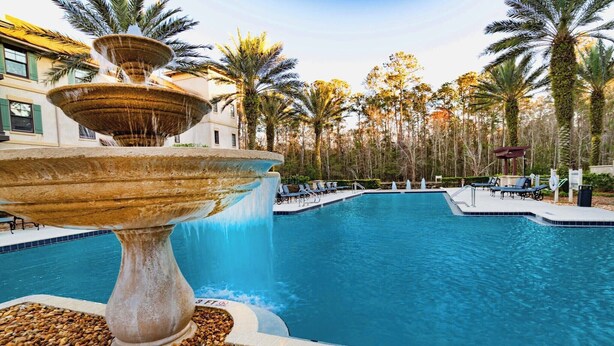 A swimming pool with a tiered fountain, surrounded by palm trees and lounge chairs.