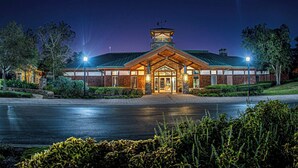A well-lit hotel entrance with a prominent tower, paved driveway, and landscaped surroundings.
