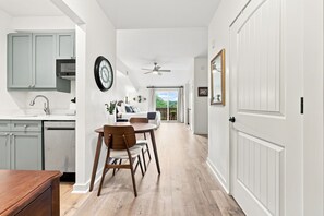 A modern kitchen with a built-in oven, a dining area with a wooden table and chairs, and a hallway leading to a door.