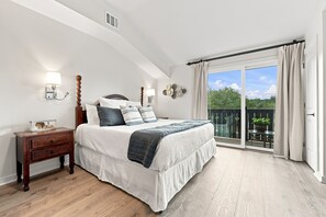 Ein Schlafzimmer mit einem großen Bett, einem Nachttisch, einer Wandlampe und Blick auf einen Balkon mit einer Glastür.