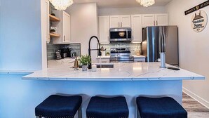 Una cocina moderna con una isla central, electrodomésticos de acero inoxidable e iluminación colgante.