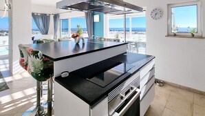 Una cocina moderna con una isla grande, electrodomésticos de acero inoxidable y vistas al mar.