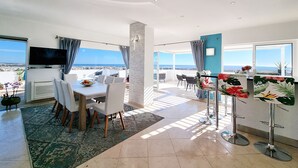 Un comedor moderno con una gran mesa y sillas, un televisor de pantalla plana y vista al océano.