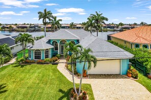 A residential property with a garage, a well-maintained lawn, and a view of a body of water. - Villa Lago Vista - Waterfront Gem w/ Gulf Access (CAPE CORAL)