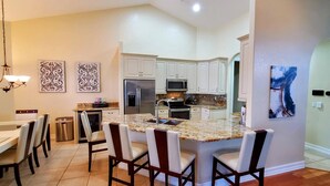 A modern kitchen with white cabinets, a granite island, and a dining area with a chandelier.