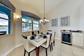 Uma sala de jantar com mesa de vidro, cadeiras, lustre e arte decorativa na parede.