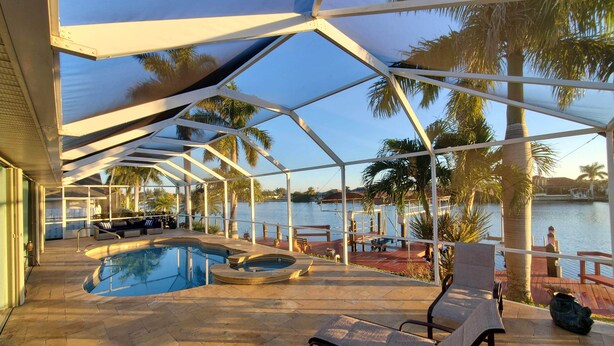 A covered outdoor swimming pool area with lounge chairs and a view of the water.