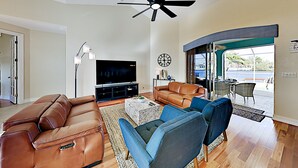 A spacious living room with leather sofas, a flat-screen TV, a ceiling fan, and a view of the outdoors.