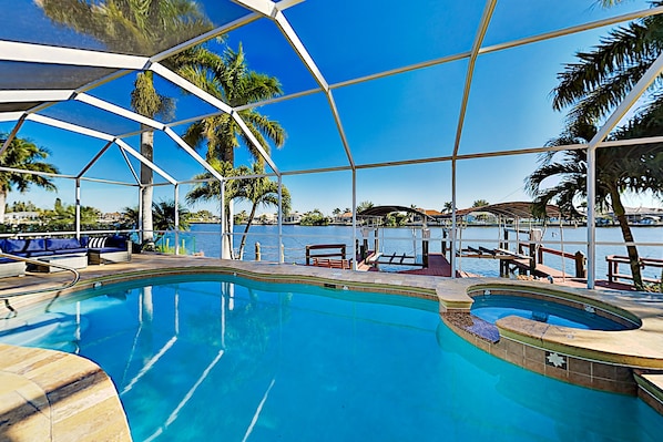Uma área de piscina com vista clara para a água, cadeiras de descanso e um espaço de estar coberto.