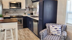 Een keuken met witte kasten, een zwart aanrecht, roestvrijstalen apparatuur en een gestreept stoel.