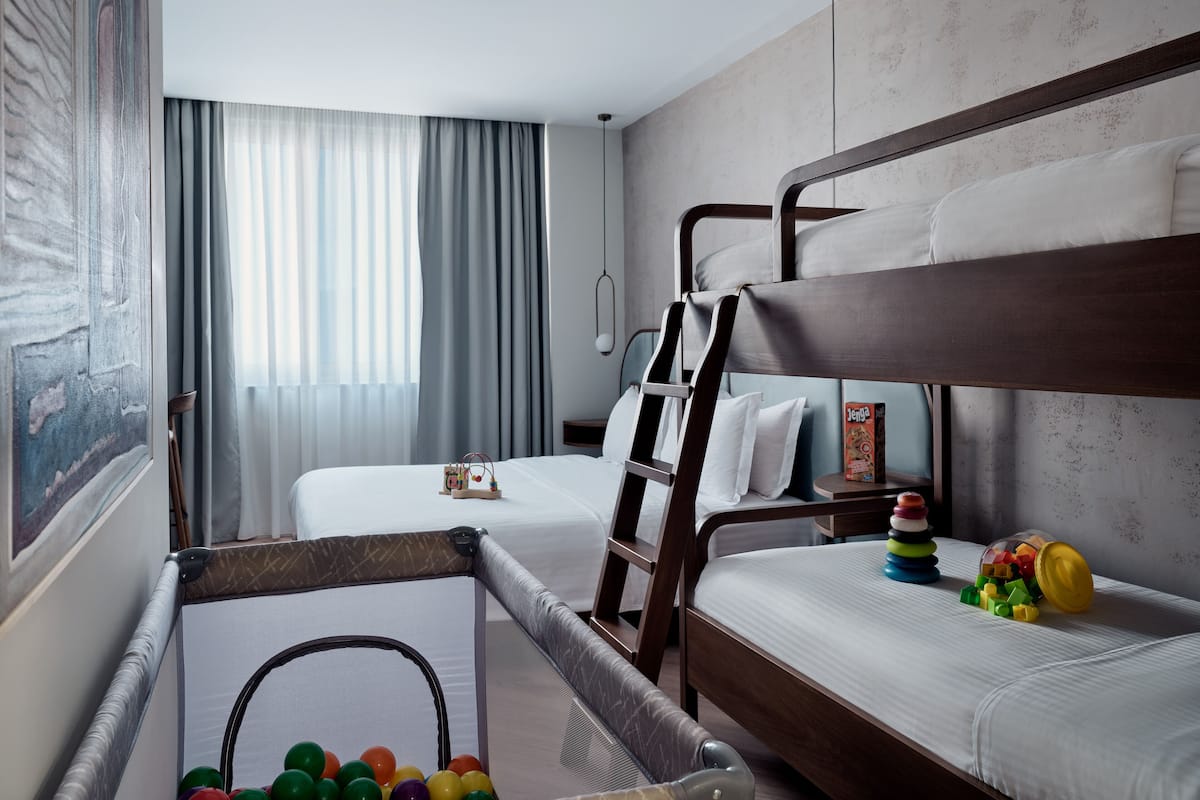 A hotel room with bunk beds, a playpen with toys, and a large window with curtains.