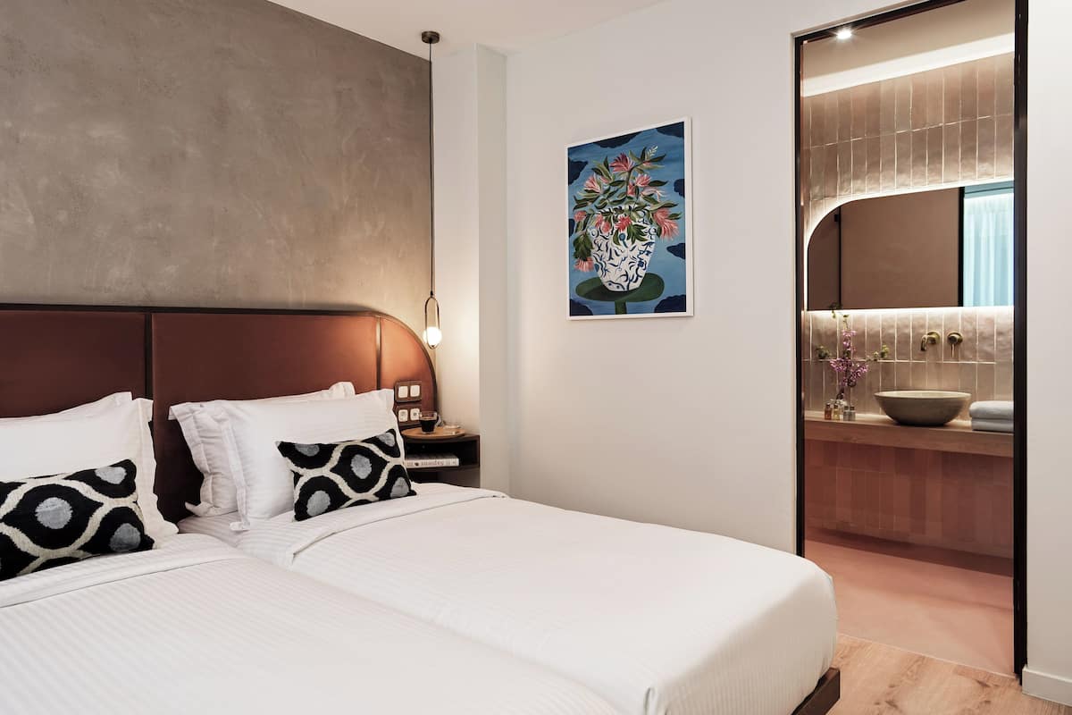 A modern bedroom with a large bed, a nightstand with a lamp, and a bathroom visible through an open door.