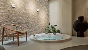 Un espace de détente avec un mur en pierre, une chaise en bois, un jacuzzi et une sculpture moderne.