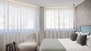 Une chambre moderne avec un grand lit, un fauteuil en forme de poire et des rideaux légers.