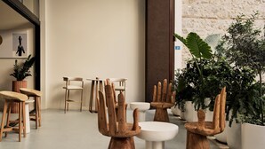 Un intérieur moderne avec des chaises en bois et une table ronde, des plantes en pot et un mur en pierre.