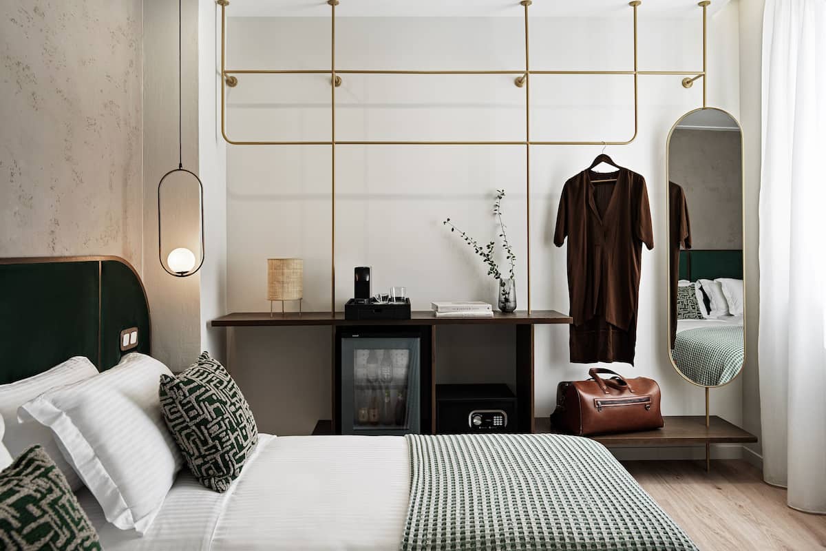 A modern hotel room with a bed, bedside table, dresser, mirror, and a hanging light fixture.