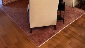 Een woonkamer met een beige bank, gestreept fauteuils, een rood tapijt en een lijst met een afbeelding aan de muur.