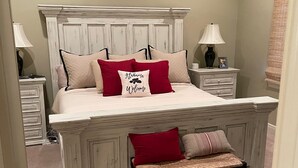 Een slaapkamer met een groot bed, een bankje, twee nachtkastjes en een plafondventilator.