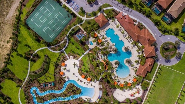 Vue aérienne d’un complexe hôtelier doté d’une grande piscine, d’un court de tennis et d’un toboggan aquatique sinueux.