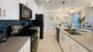 A modern kitchen with stainless steel appliances, white cabinetry, and a large island with a sink.