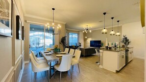 A modern kitchen with a dining area, large windows, and a TV.