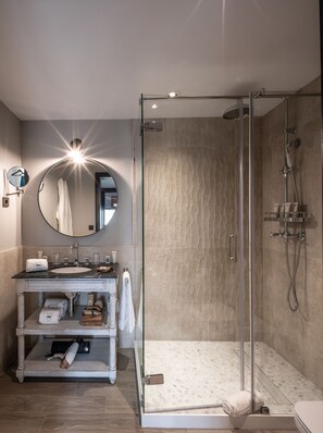 A modern bathroom with a glass-enclosed shower, a round mirror, and a vanity with a marble countertop. - Hotel El Castillo La Ciudadela Marbella (Marbella)