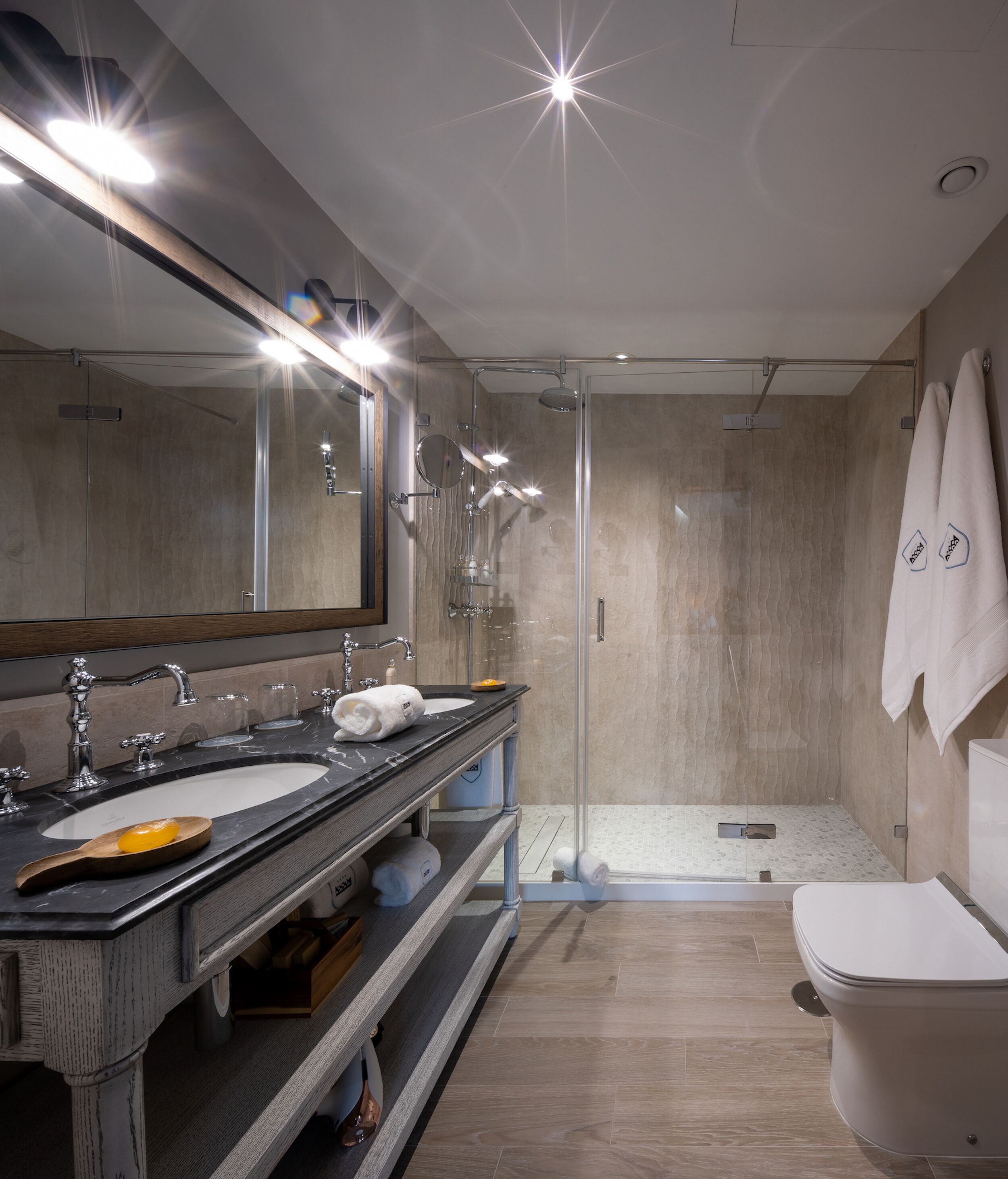 Une salle de bain moderne avec deux vasques, un grand miroir, une douche à l’italienne et des toilettes.