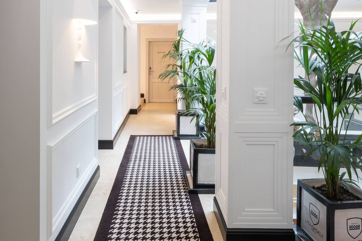 A hallway with patterned carpets, potted plants, and a statue.