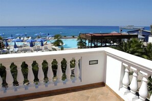 Un área de piscina con sillones de playa y sombrillas, vista al océano y un edificio con techo rojo.