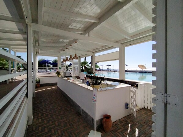 An outdoor bar area with a pool view, white railings, and hanging lights.