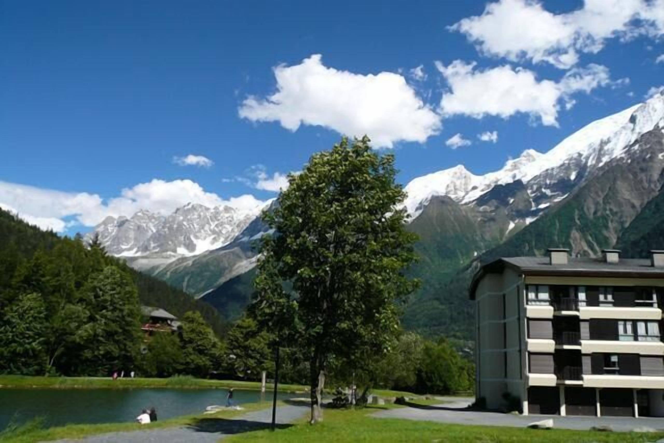 A building with a modern design, situated in a mountainous area with a lake and snow-capped peaks in the background.