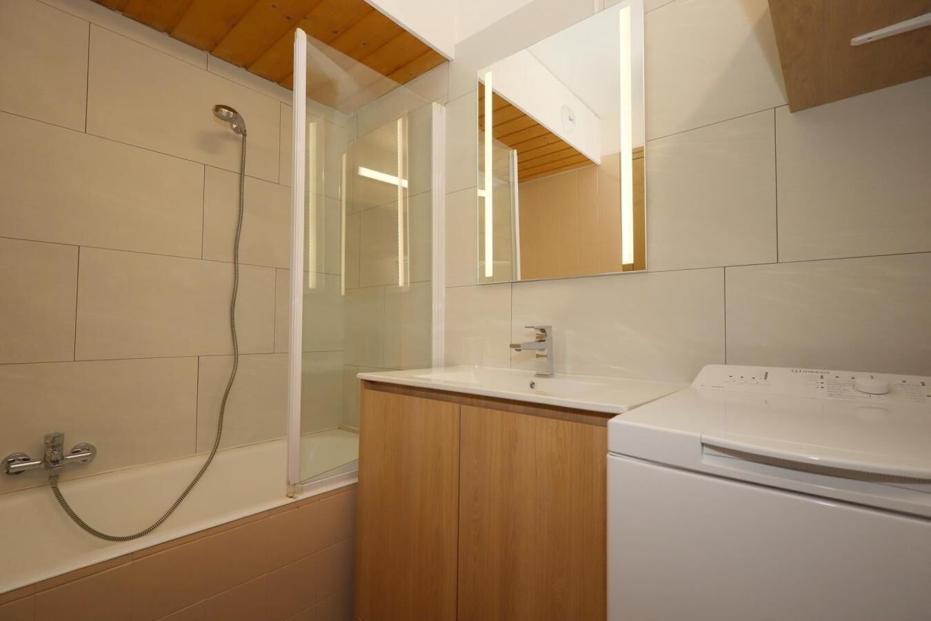 A modern bathroom with a glass-enclosed shower, a wooden vanity, and a built-in washing machine.
