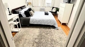 Una camera da letto con un letto, una ventola a soffitto, una TV, una cassettiera e una finestra con tende.