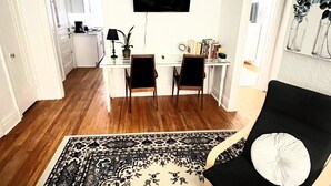 Un soggiorno moderno con un tappeto a motivi bianco e neri, un divano nero con un cuscino bianco, e una zona pranzo con due sedie e un piccolo tavolo.