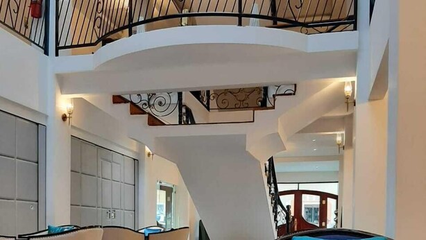 A spacious lobby with a curved seating area, a piano, and a staircase with a black railing. - L'ver Hotel (Somoto)
